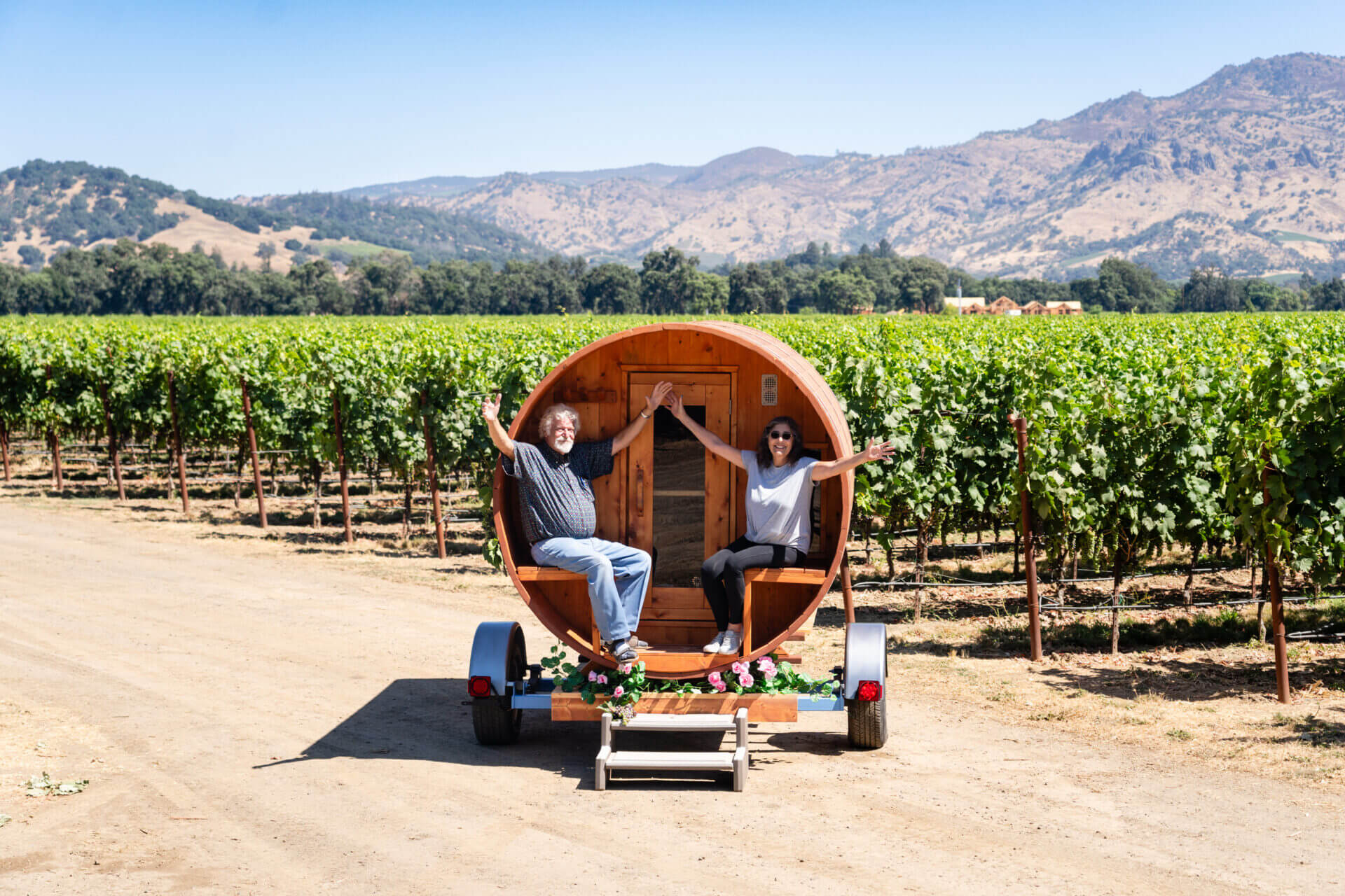 Two people sitting in a barrel on the back of a trailer.